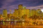 Stock photo of the Calgary skyline of high-rise buildings, the Calgary Tower, and the Centre Street Bridge spanning the Bow River at dusk in the City of Calgary, Alberta, Canada. the clouds above the illuminated city are dark as the sun sets over the larg