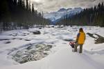 Stock photo of a woman with snowshoes looking at the snow covered winter landscape surrounding the Mistaya River with Mount Sarbach in the background, Mistaya Canyon, Icefields Parkway, Banff National Park, Canadian Rocky Mountains, Alberta, Canada.