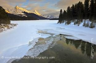 Stock photo of the partially frozen Maligne River as it drains from Maligne Lake during winter with a view towards the snow capped mountains of Leah Peak (2810 metres/9220 feet) and Samson Peak (3077 metres/10095 feet) during sunset, Maligne Lake Road, Ja