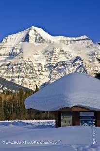 Stock photo of Snow-capped Mount Robson towering over a heavily snow covered visitor information kiosk against a bight blue sky in Mount Robson Provincial Park, British Columbia, Canada. 