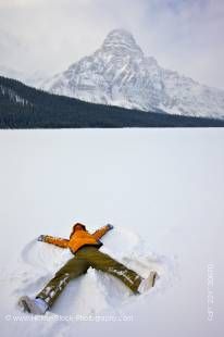 Stock photo of woman making snow angel on Waterfowl Lake after fresh snowfall with Mount Chephren towering into the background sky. 